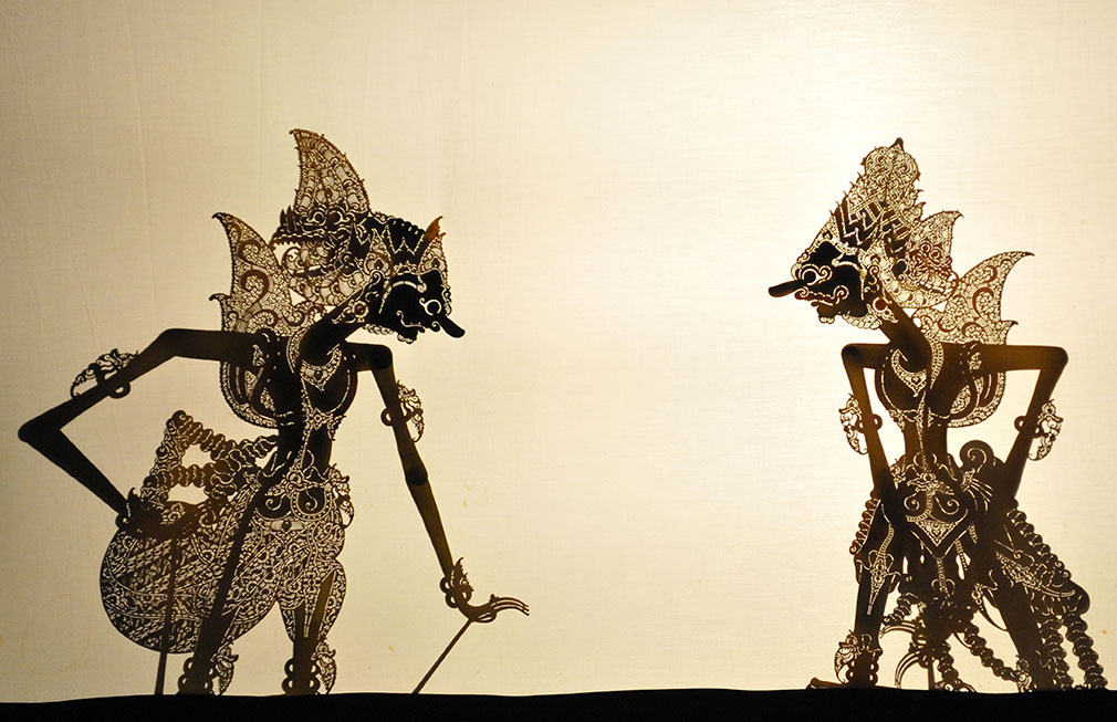A traditional Indonesian performance of Wayang kulit, with two intricately designed shadow puppets.