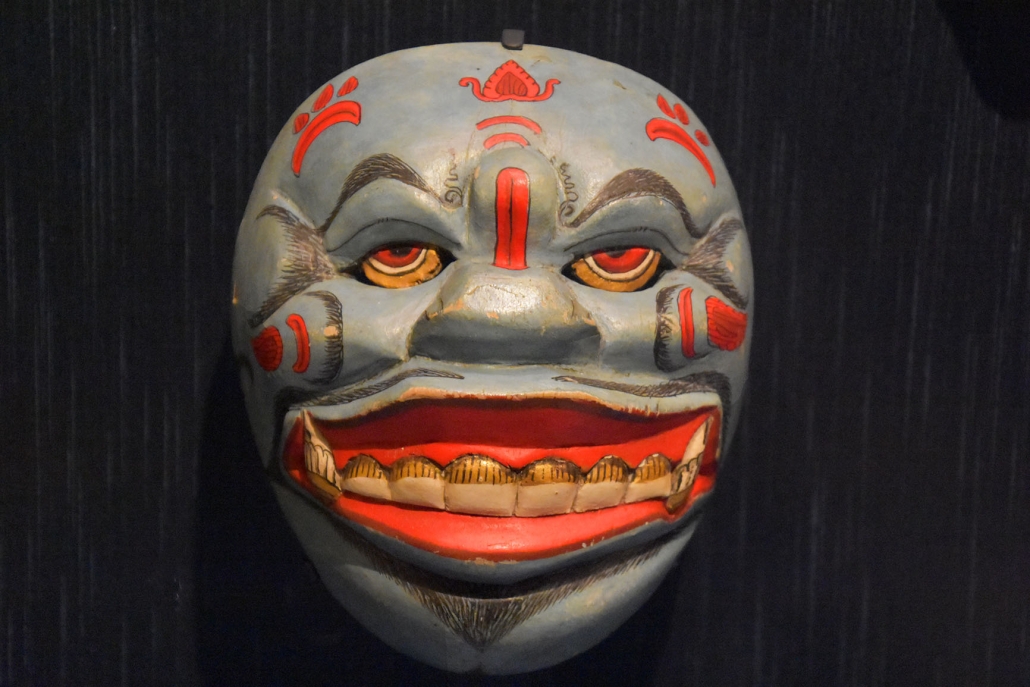 A traditional Indonesian mask, with red and white paint and large teeth, used in ritual ceremonies.