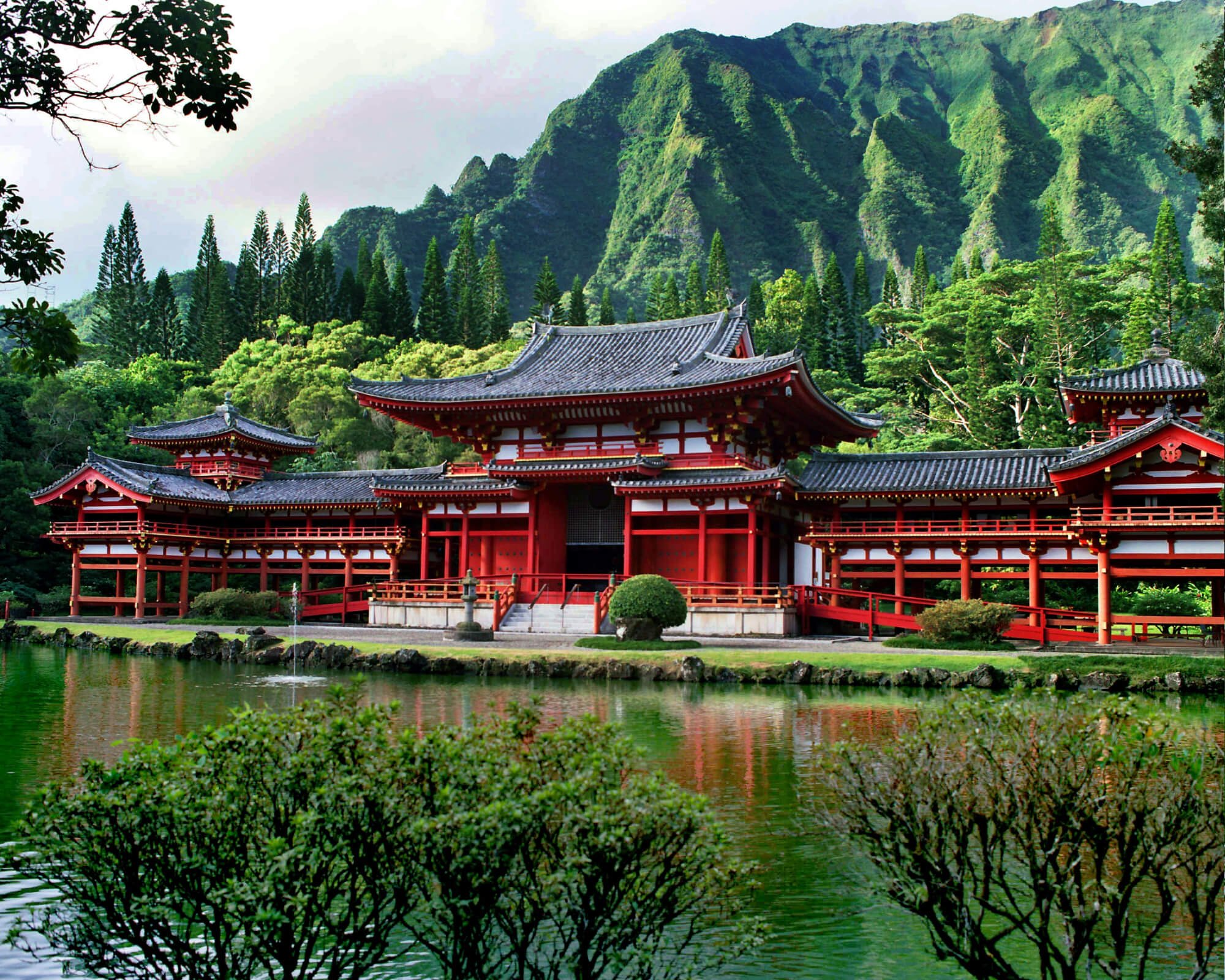 A Buddhist temple with intricate details is surrounded by lush green mountains and a tranquil reflecting pond.