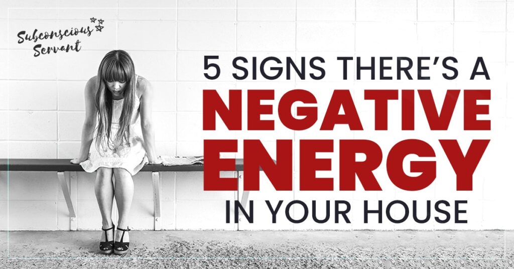 A woman sits on a bench in front of a brick wall with her head in her hands next to the text: '5 Signs There's Negative Energy In Your House'.