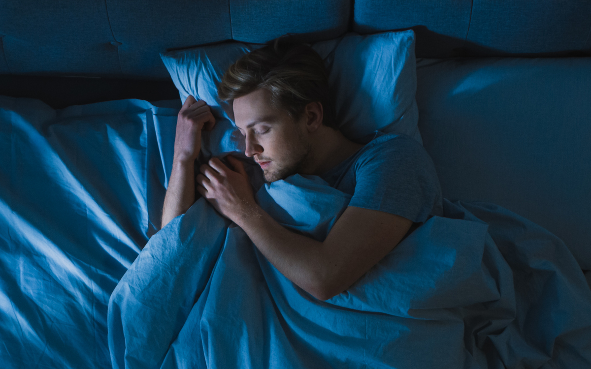 A man is sleeping in his bed, unaware of the ghost standing beside him.