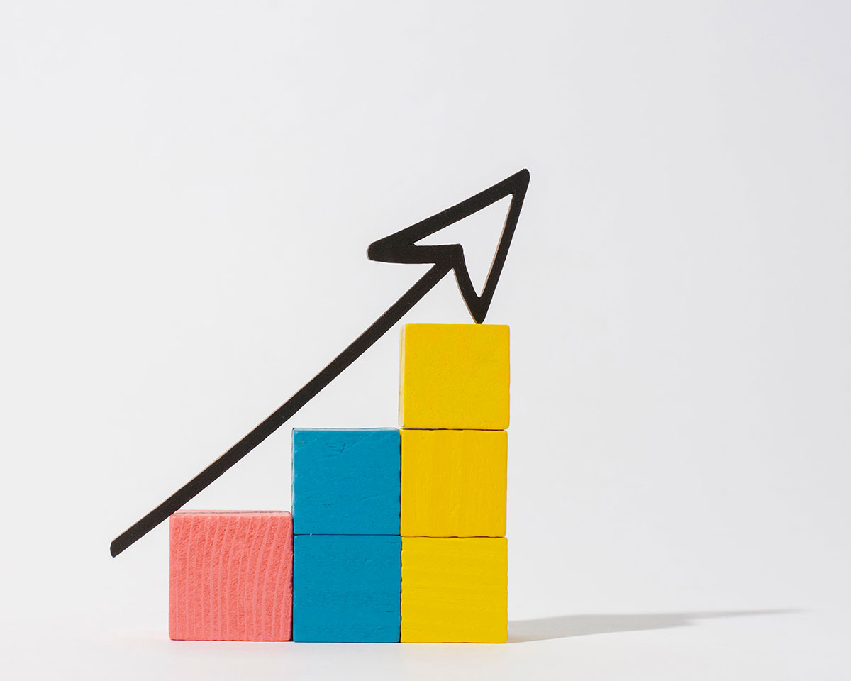 A bar graph made of three blocks painted in pink, blue, and yellow with a black arrow on top to symbolize increasing sales with ilmu pelaris.