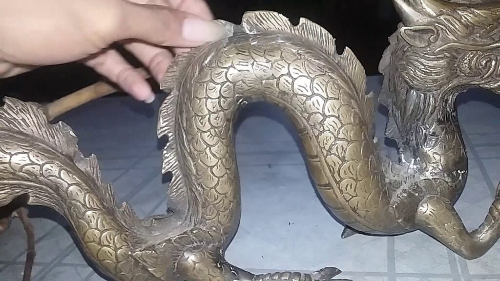 A hand holding a traditional Javanese pusaka heirloom made of bronze in the form of a dragon with intricate details.