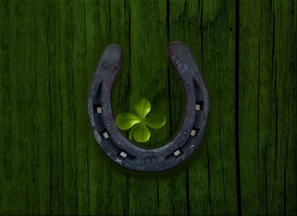 A horseshoe with a four-leaf clover in the center is mounted on a wooden background.