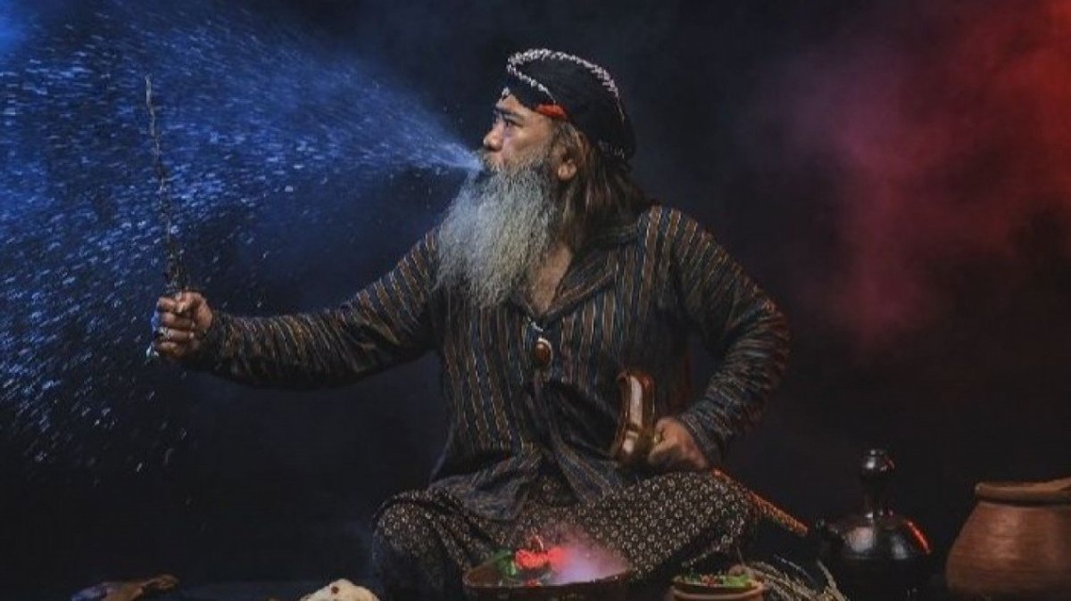 A dukun, or traditional Indonesian exorcist, is shown in a dramatic pose, spraying water from his mouth while holding a keris, a traditional Javanese dagger.