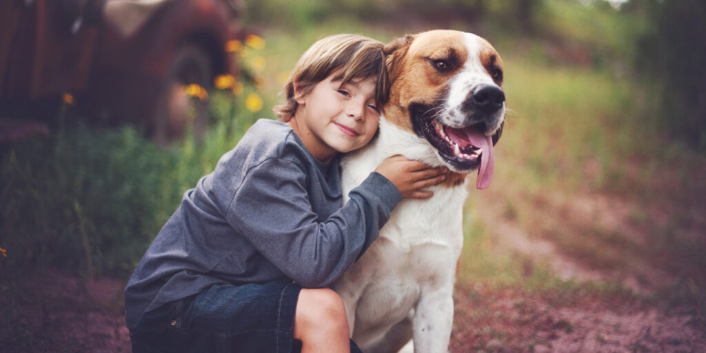 Boy with a radiant smile hugging a big dog with a compassionate aura.