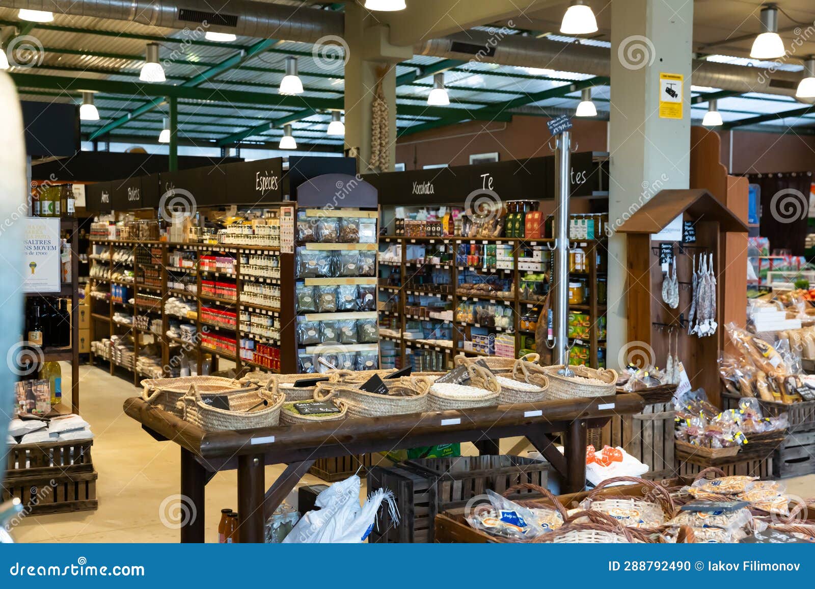 An organized grocery store with various products on the shelves and in baskets on a wooden table in the center.